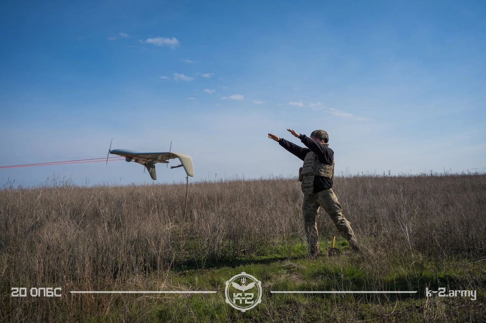Військовий запускає безпілотник літакового типу з відкритої польової ділянки під ясним небом. Кадр передає момент роботи операторів БПЛА, коли апарат уже набирає політ над сухою травою.