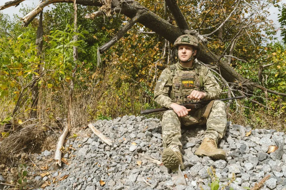 Боєць в екіпіруванні з автоматом сидить на камінні