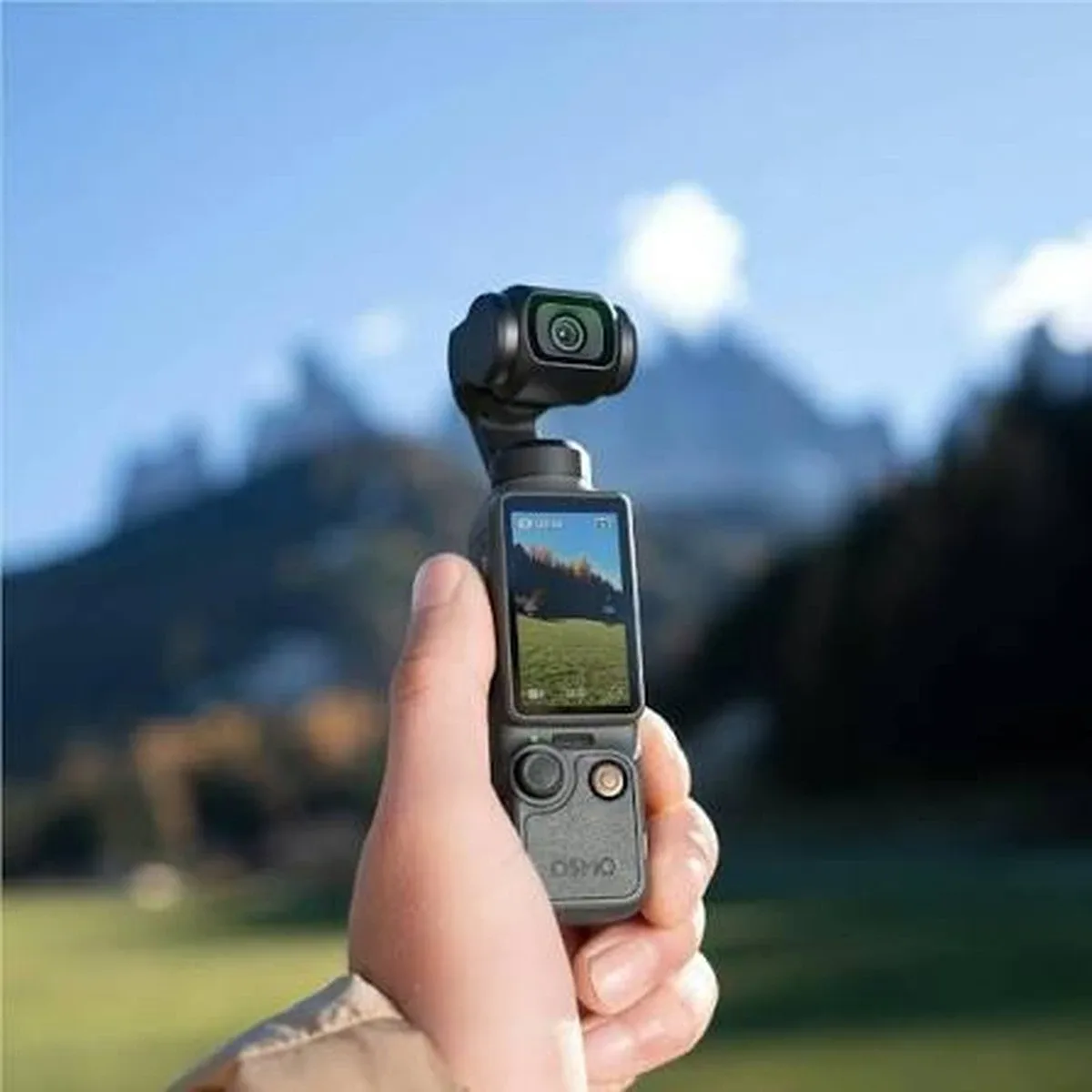 Рука тримає камеру DJI Osmo Pocket 4 з вертикально повернутим дисплеєм у сонячний день на фоні гір