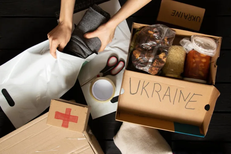Людина розпаковує набір гуманітарної допомоги, фото крупним планом. На коробці з продуктами напис Ukraine