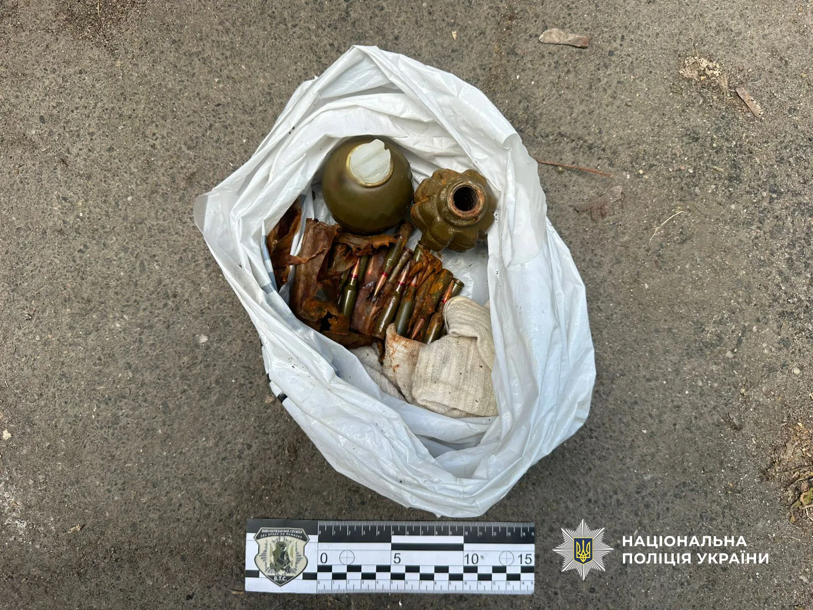 Дві ручні гранати та пачка набоїв у білому поліетиленовому пакеті на асфальті поруч із масштабною лінійкою