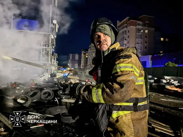 пожежник стоїть на фоні будинку, покшодженого обстрілом 