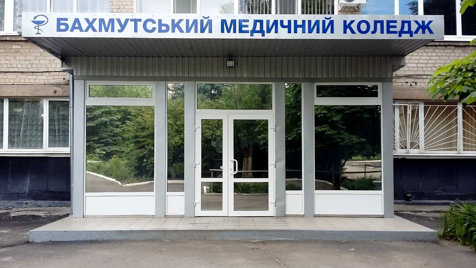 Вхід до будівлі Бахмутського медичного коледжу. Над скляними дверима розміщена велика вивіска з назвою закладу, по боках видно вікна та цегляний фасад будівлі