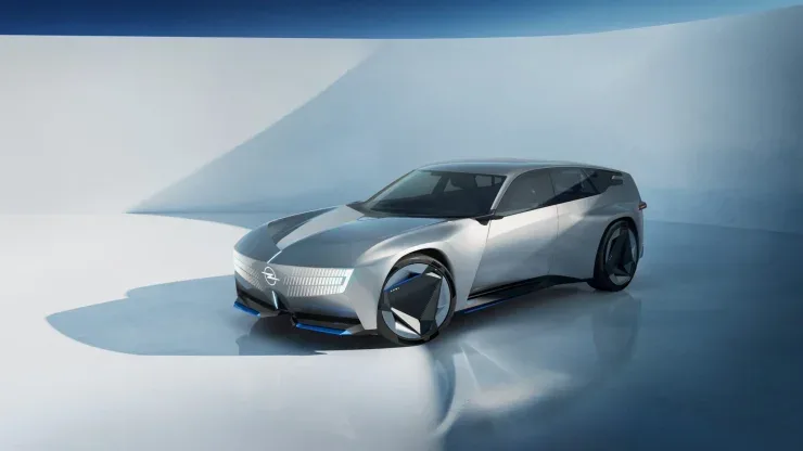 Серебристый электрический универсал Opel STX Concept с футуристическим дизайном, большими треугольными колесами и подсвеченной передней панелью Opel Vizor в выставочном зале