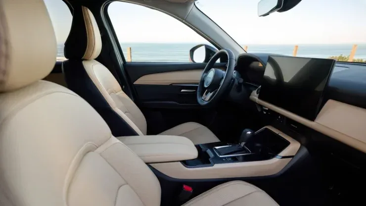 Салон кроссовера Mazda 2027 года со светлыми кожаными сиденьями и цифровым экраном мультимедиа на фоне моря