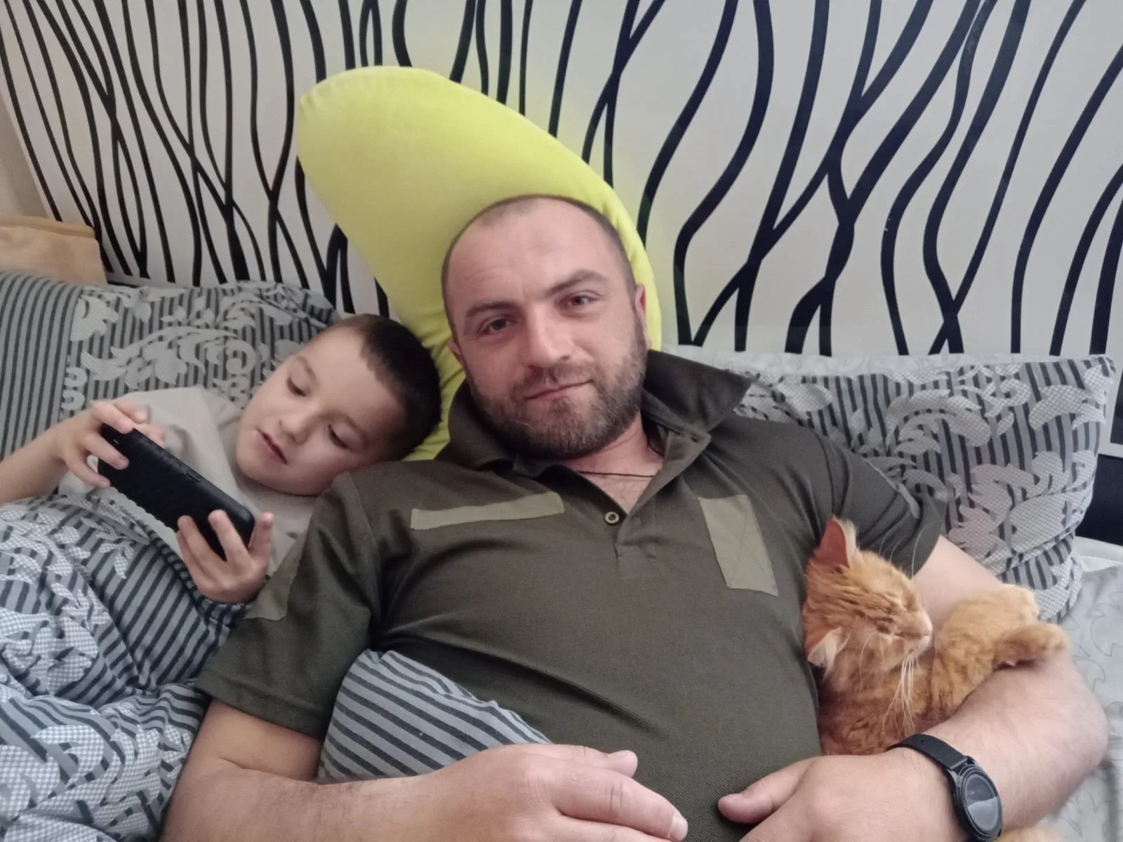 На ліжку чоловік, його син і кіт