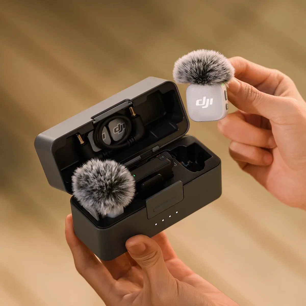 Руки тримають відкритий зарядний кейс комплекту DJI Mic Mini 2 з мікрофонами, хутряним вітрозахистом та адаптерами