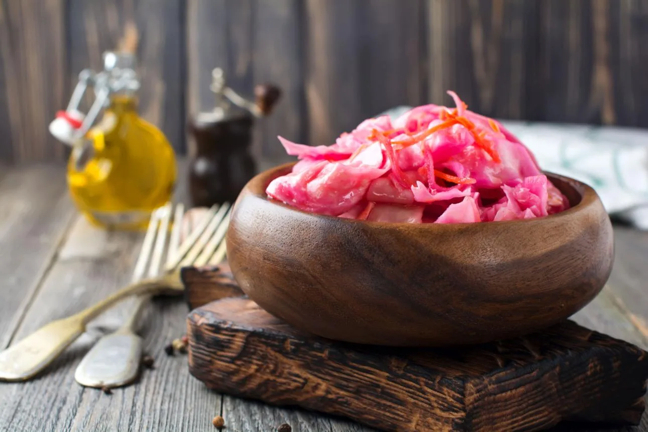 Sour cabbage with with beets and carrots in a bamboo bowl on old wooden background. Rustic style. Selective focus.