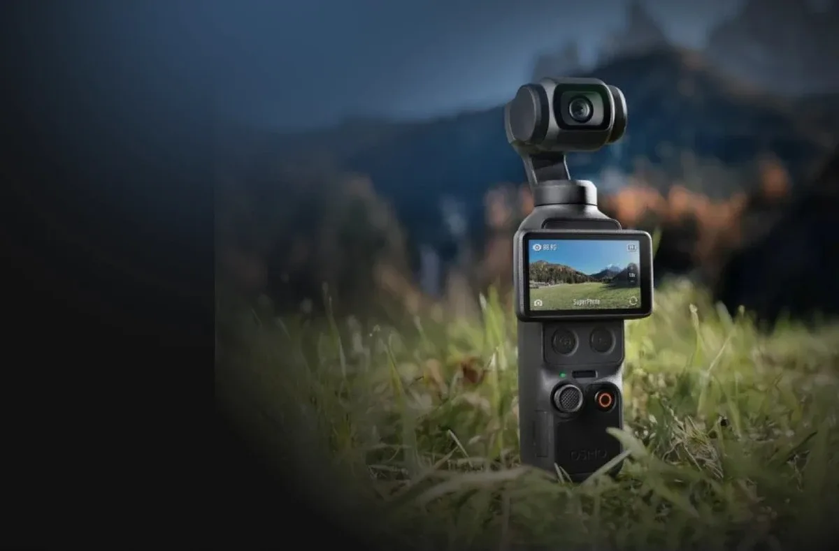 Портативна камера DJI Osmo Pocket 4 стоїть у траві на фоні вечірнього гірського лісу в режимі зйомки SuperPhoto
