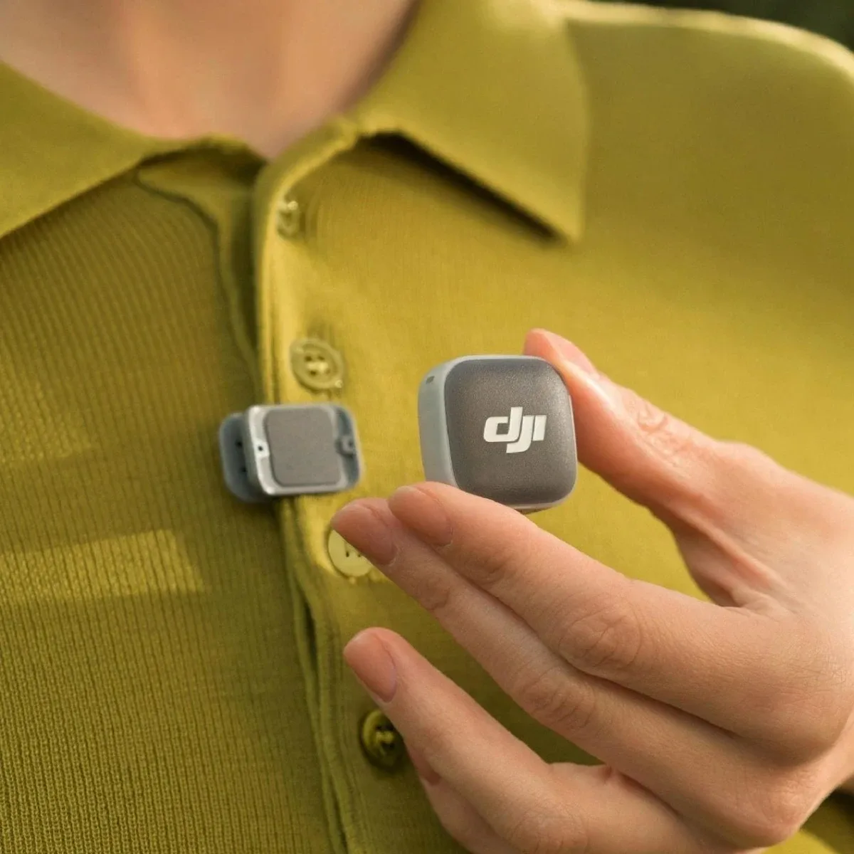 Передавач DJI Mic Mini 2 підносять до магнітної кліпси на планці сорочки оливкового кольору при денному освітленні
