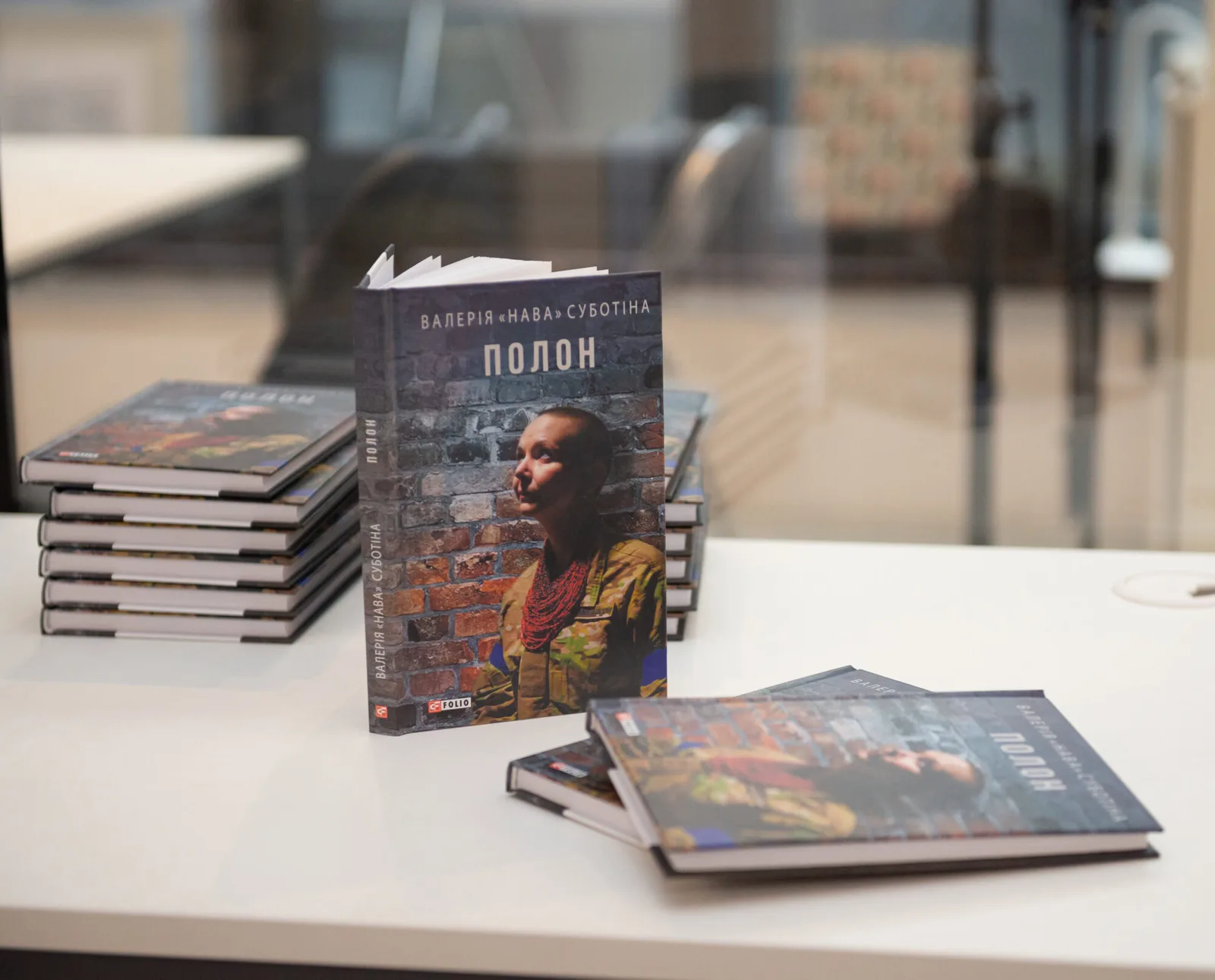 Кілька примірників книги Валерії «Нави» Суботіної «Полон» лежать на столі, один примірник стоїть вертикально. На обкладинці — портрет авторки у військовій формі на тлі цегляної стіни.