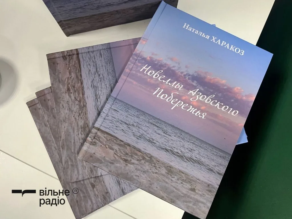 Кілька примірників книги Наталії Харакоз «Новеллы Азовского Побережья» лежать на столі. На обкладинці — фотографія Азовського моря та узбережжя на тлі рожево-блакитного неба.